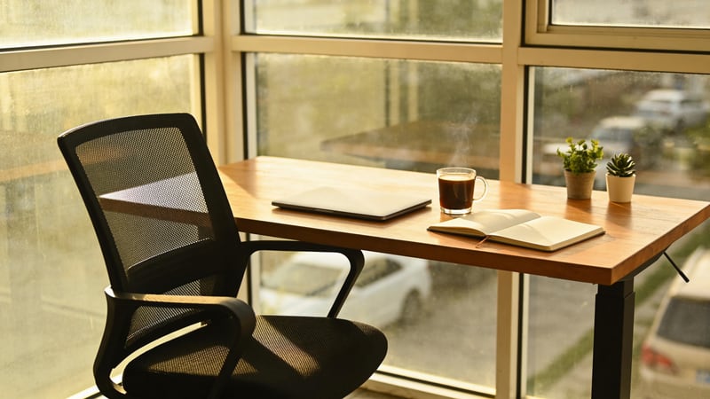 Ruhiger Arbeitsplatz mit geschlossenem Laptop, Kaffee und leerem Stuhl am Fenster im warmen Spätnachmittagslicht — abgesichert mit der BarmeniaGothaer Berufsunfähigkeitsversicherung