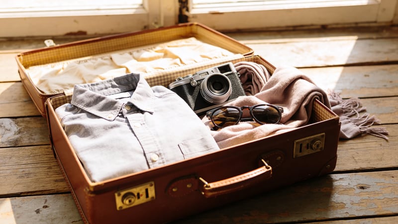 Halb-offener Vintage-Lederkoffer mit Kamera, Kleidung und Sonnenbrille auf Holzboden — abgesichert mit der Barmenia Reisegepäckversicherung